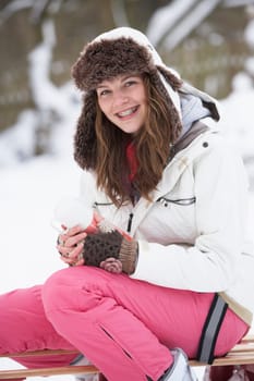 Teenage Girl Sitting On Sledge With Flask And Hot Drink