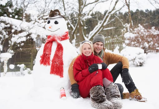 Teenage Couple In Winter Landscape Next To Snowman With Flask And Hot Drink