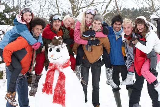 Group Of Teenage Friends Building Snowman In Garden