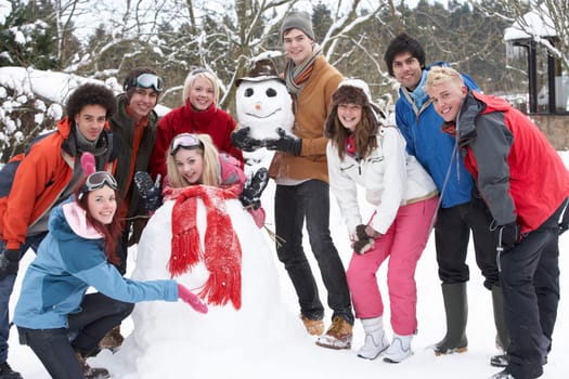 Group Of Teenage Friends Building Snowman In Garden