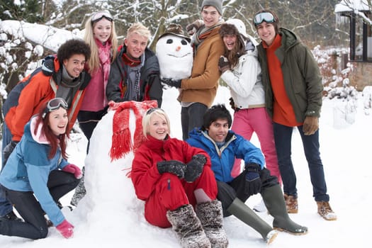 Group Of Teenage Friends Building Snowman In Garden