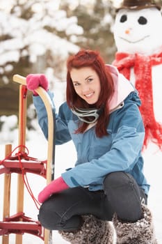 Teenage Girl With Sledge Next To Snowman