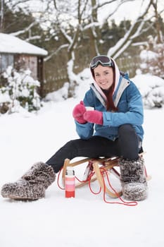 Teenage Girl With Sledge Next To Snowman With Flask And Hot Drink
