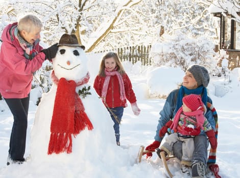 Young Girl With Grandmother And Mother Building Snowman In Garden