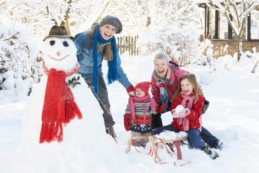 Young Girl With Grandmother And Mother Building Snowman In Garden