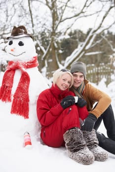 Teenage Couple In Winter Landscape Next To Snowman With Flask And Hot Drink