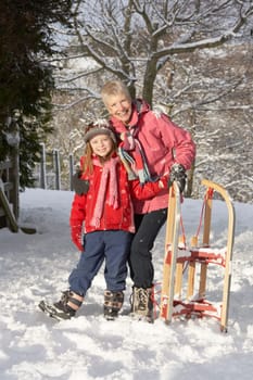 Young Girl With Grandmother Holding Sledge In Snowy Landscape