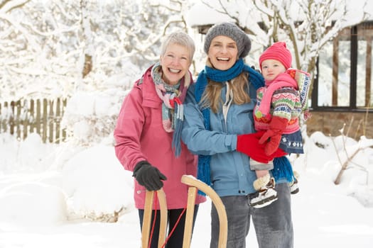 Young Girl With Grandmother And Mother Holding Sledge In Garden