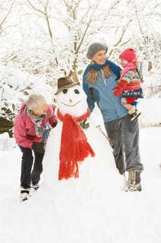 Young Girl With Grandmother And Mother Building Snowman In Garden