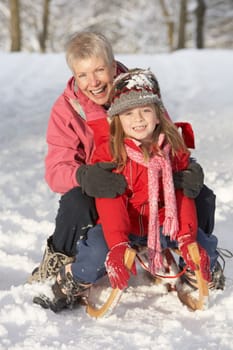 Young Girl With Grandmother Riding On Sledge In Snowy Landscape