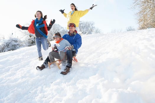Family Having Fun Sledging Down Snowy Hill
