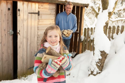 Father And Daughter Collecting Logs From Wooden Store In Snow