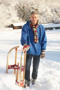 Middle Aged Man Standing In Snowy Landscape Holding Sledge