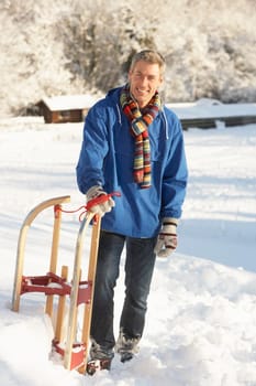 Middle Aged Man Standing In Snowy Landscape Holding Sledge