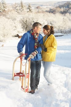 Young Couple Standing In Snowy Landscape Holding Sledge