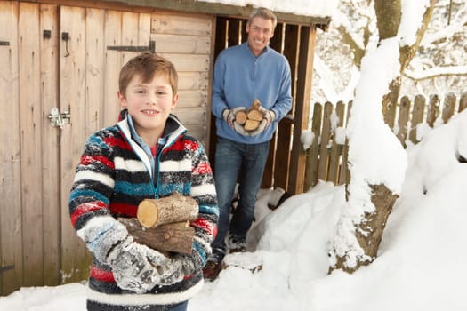 Father And Son Collecting Logs From Wooden Store In Snow
