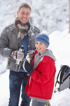 Father And Son Stopping For Hot Drink And Snack On Walk Through Snowy Landscape
