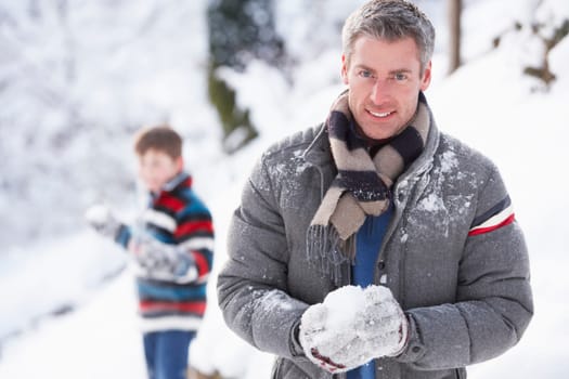 Father And Son Having Snowball Fight In Winter Landscape
