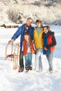 Young Family Standing In Snowy Landscape Holding Sledge