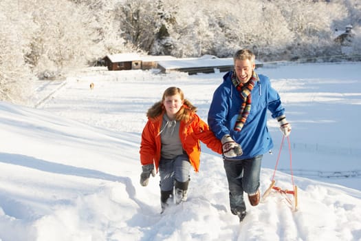 Father And Son Pulling Sledge Up Snowy Hill