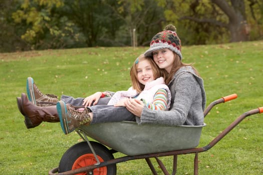 Two Sisters Sitting In Wheelbarrow Outdoors