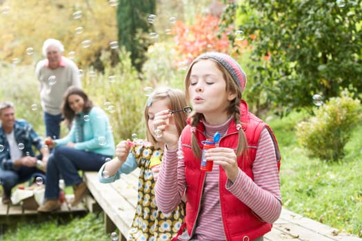 Two Young Girls Blowing Bubbles On Countryside Picnic