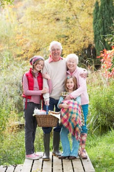 Grandparents With Grandchildren Carrying Picnic Basket By Autumn Woodland