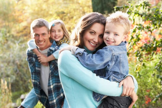 Family Group Outdoors In Autumn Landscape With Parents Giving Chiildren Piggybac