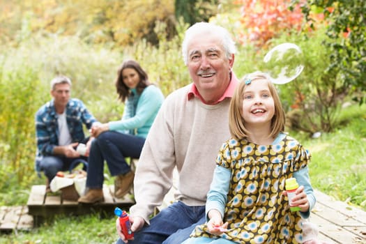 Grandfather And Granddaughter Blowing Bubbles On Family Picnic