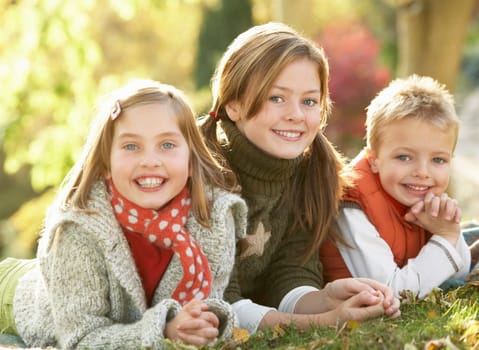 Group Of 3 Children Realxing Outdoors In Autumn Landscape