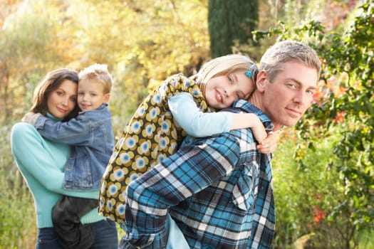 Family Group Outdoors In Autumn Landscape With Parents Giving Chiildren Piggybac