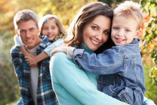 Family Group Outdoors In Autumn Landscape With Parents Giving Chiildren Piggybac