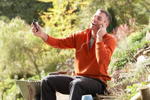 Man Outdoors Listening To MP3 Player Whilst On Break From Gardening