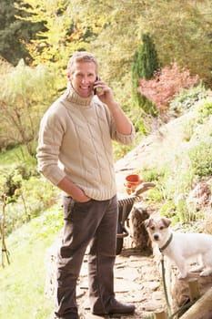 Man Outdoors On Mobile Phone With Dog Whilst On Break From Gardening
