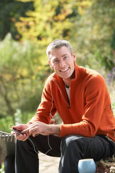 Man Outdoors Listening To MP3 Player Whilst On Break From Gardening