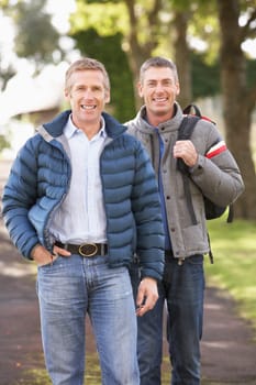 Two Male Friends Walking Outdoors In Autumn Park Together