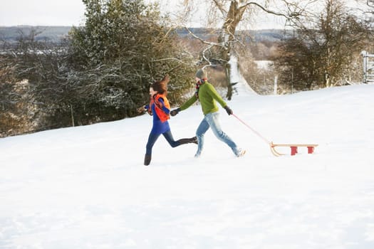 Teenage Couple Pulling Sledge Across Snowy Field