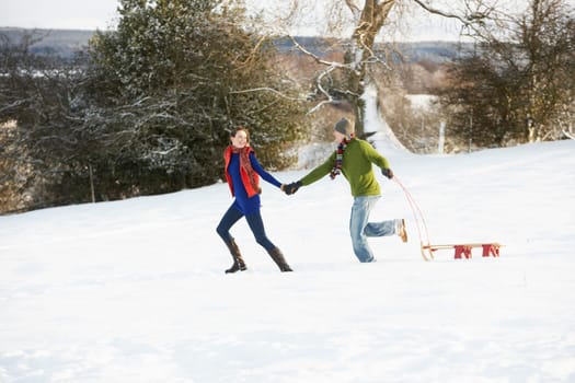 Teenage Couple Pulling Sledge Across Snowy Field