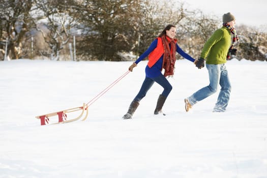 Teenage Couple Pulling Sledge Across Snowy Field