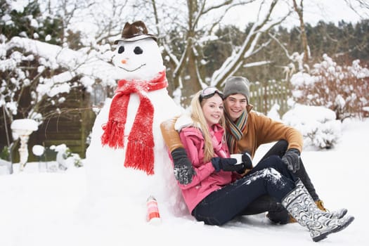 Teenage Couple In Winter Landscape Next To Snowman With Flask And Hot Drink