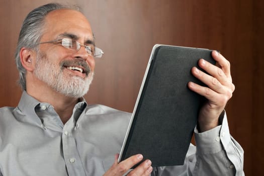 Portrait of a smiling businessman reading information from an electronic tablet. Horizontal shot.