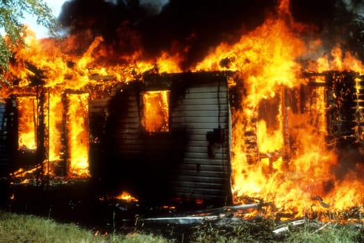 A house is fully engulfed in flames as it burns out of control to the ground. Horizontal shot.