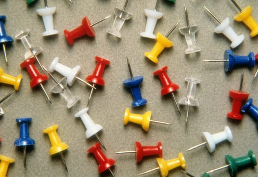 Different colors of pushpins scattered on a counter top. Horizontal shot.