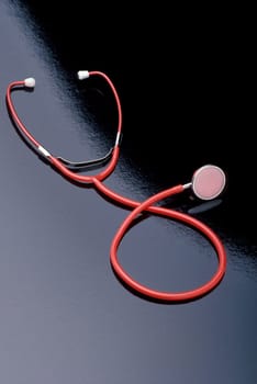 A red stethoscope is laying on a black reflective surface. Vertical shot.