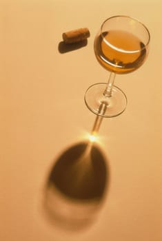 High angle view of a cork and a glass of wine. Light is being magnified through the glass stem, causing a point of light on the shadow. Vertical shot