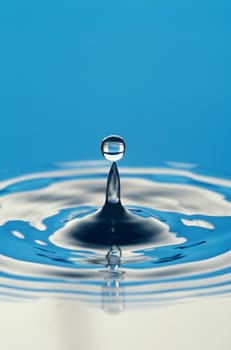 Close-up of a water droplet falling onto a calm water surface, creating a splash and ripples. Vertical shot