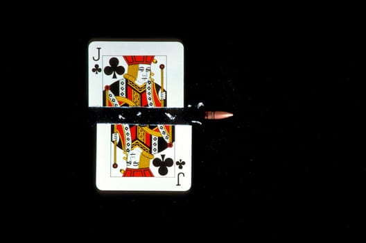A jack of clubs is shown being shot in half by a bullet. Horizontal shot.