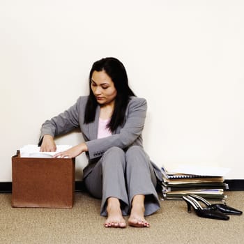 A young businesswoman is sitting on the floor with her shoes off and looking through a file folder. Square shot.