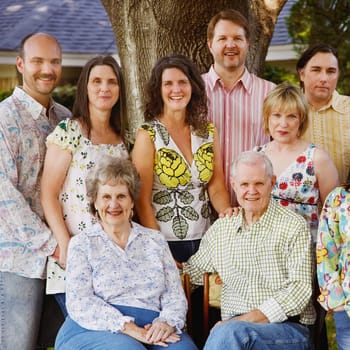 A multi-generation family is standing under a tree at a family reunion. Square shot.