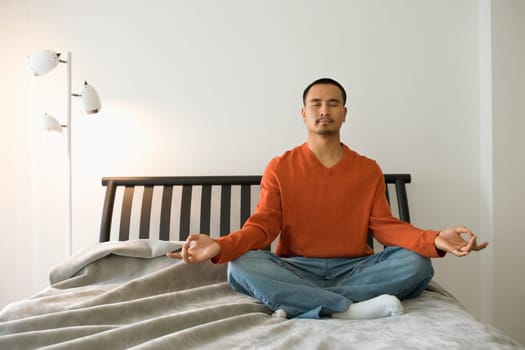 Young man sitting on bed in the lotus position. Horizontal shot.